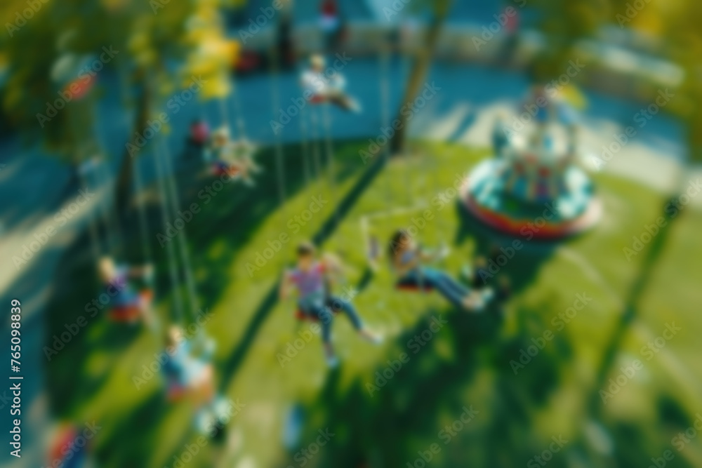 blurred image of children on carousel against the backdrop of bright green park on sunny day