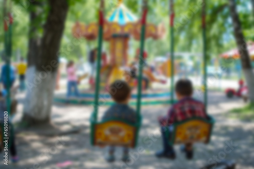 Blurred image of children on swing against the backdrop of bright green park on sunny day