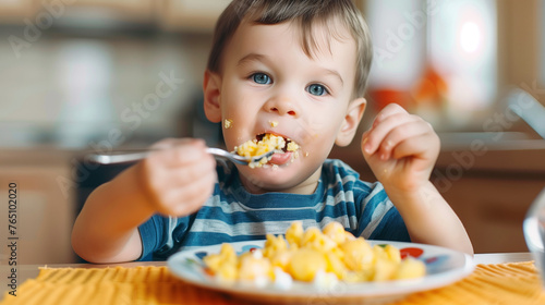 funny boy has Breakfast crumbled eggs alone with a spoon and make a mess, cute funny boy eating eggs by himself.