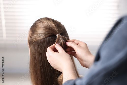 Professional stylist braiding woman's hair indoors, closeup