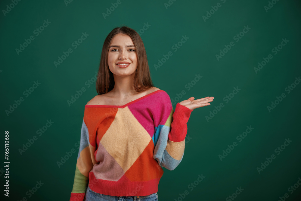Showing by hand to the side, place for text. Young woman is standing against green background in the studio Showing by hand to the side, place for text. Young woman is standing against green background in the studio