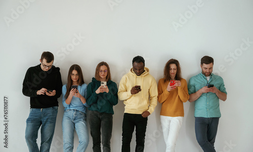 Joyful, holding smartphones. Group of young people are standing against white background