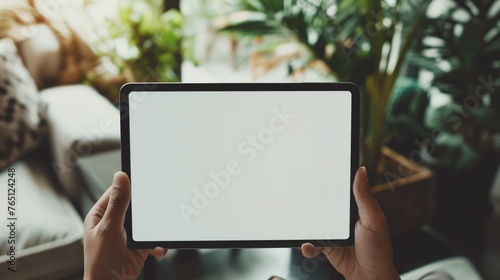 Woman holding a digital tablet with a blank screen in a home interior with a blurred background.