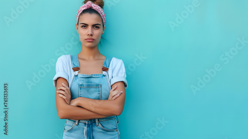 Portrait of awhite woman wearing denim overalls standing against blue wall