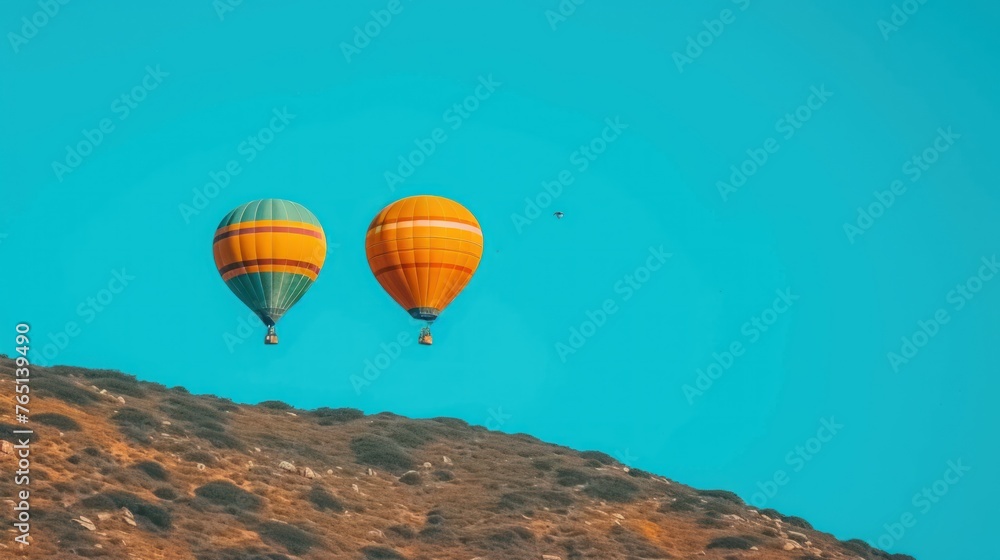 Obraz premium a couple of hot air balloons flying in the sky over a mountain side with a bird flying in the distance.