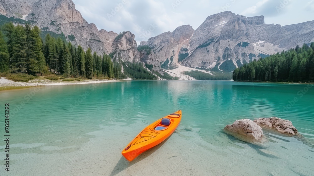 an orange kayak sitting on the shore of a lake in front of a mountain range with pine trees in the foreground.