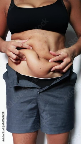 overweight fat woman wearing gray shorts, moving and tightening her belly with excess weight and sagging on white background.