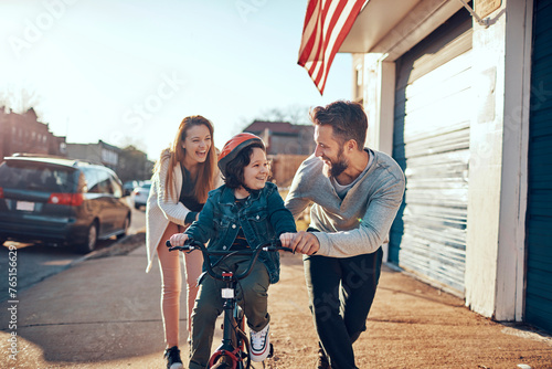 Happy family teaching child to ride a bicycle outdoors
