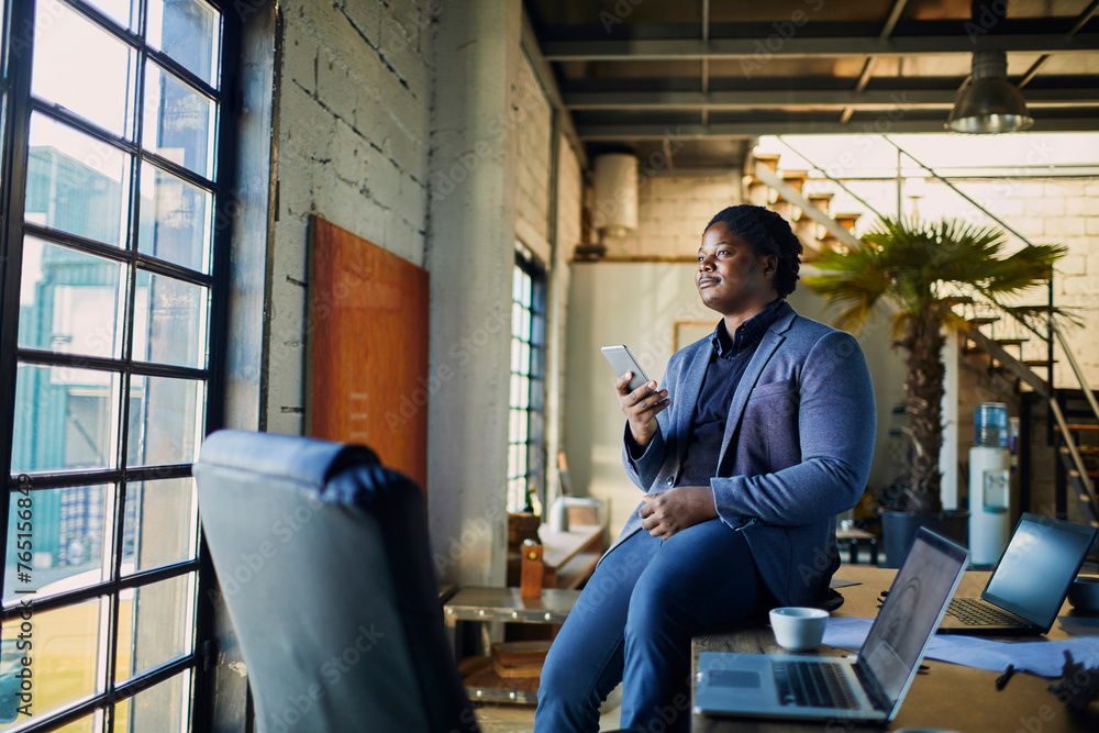 Businessman with smartphone sitting on desk with laptops in modern loft office Businessman with smartphone sitting on desk with laptops in modern loft office