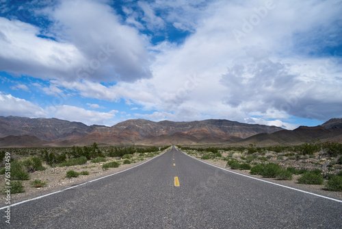 Road less traveled shown in the Mojave Desert in California, USA, in mid-March 2024. Road on a barren landscape with blue skies and puffy white clouds. Road forms a vanishing point.
