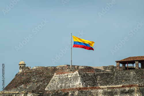 Cartagena, Colombia - July 25, 2023: Gray-beige stone San Felipe de Barajas Fort with national flag against blue sky photo
