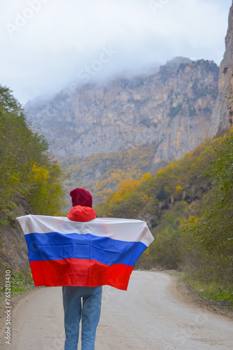 Obraz na płótnie Woman traveler on a winding road in the mountains on a foggy autumn day with the flag of the Russian Federation on her shoulders w salonie