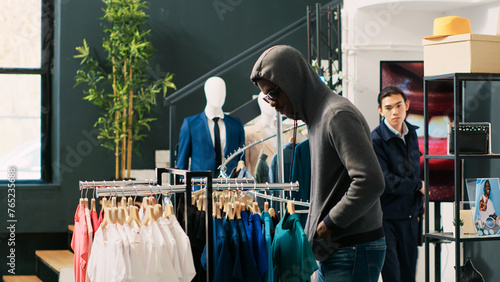 African american robber trying to steal stylish clothes, being threatened with security baton buy asian bodyguard in modern boutique. Thief wearing sunglasses and hood not to be recognized
