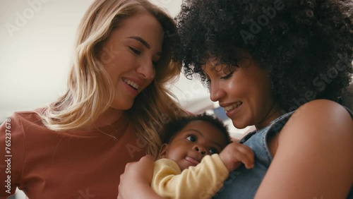Same sex female couple or friends playing with baby sitting on sofa at home together - shot in slow motion