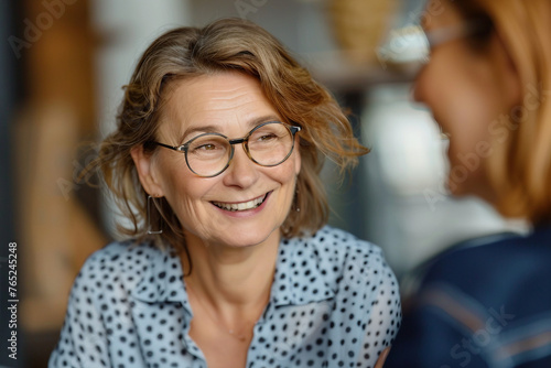 Smiling aged businesswoman in glasses looking at colleague at team meeting happy attentive female team leader listening to new project idea coach mentor teacher excited by interesting discussion