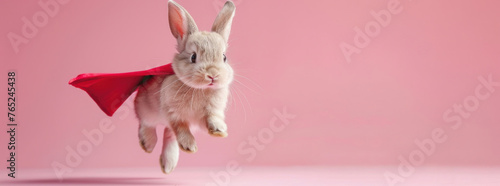 baby bunny rabbit wearing cloak jumping and flying with copy space on pastel pink color background photo