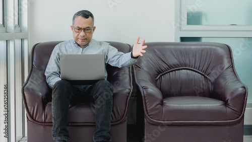 A man is sitting on a leather chair with a laptop in front of him