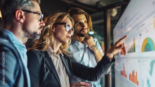 Creative Team Analyzing Project Data on Interactive Display. Engaged professionals pointing at interactive data charts, collaborating on strategic planning in a high-tech office environment.