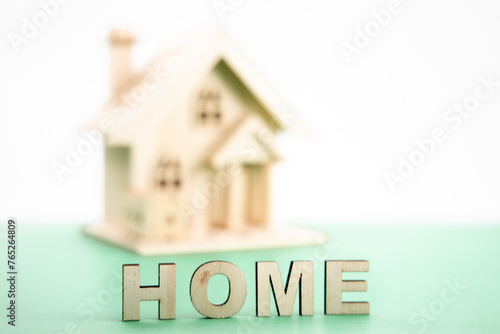 The word HOME spelled out in wooden letters with an out of focus model wooden house in the background