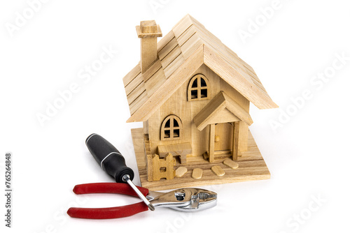A wooden model of a house with handiman tools, a screw driver and pliers, suggesting a real estate maintenance and repair costs or chores photo