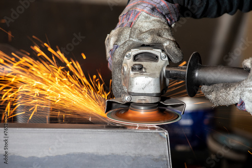 An industrial hand grinder grinding a welded joint to smooth and remove burr with a shower of sparks