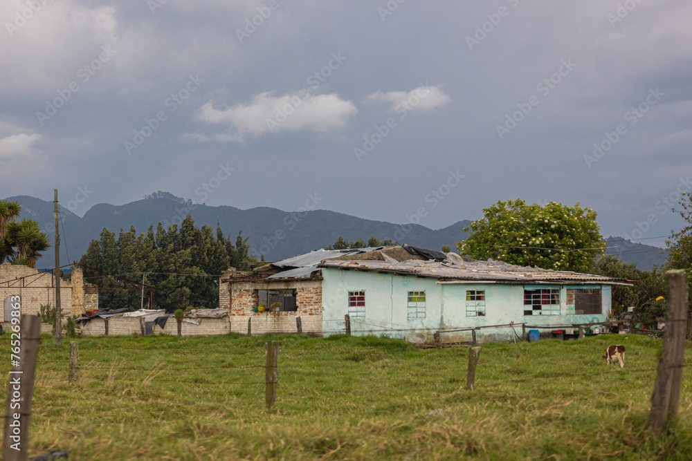exterior of a poor house in the countryside with trees and mountains in the background 