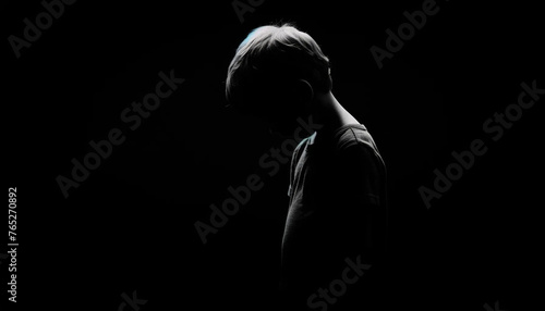  The silhouette of a sad little boy, his shoulders slumped and head bowed, against a deep black background