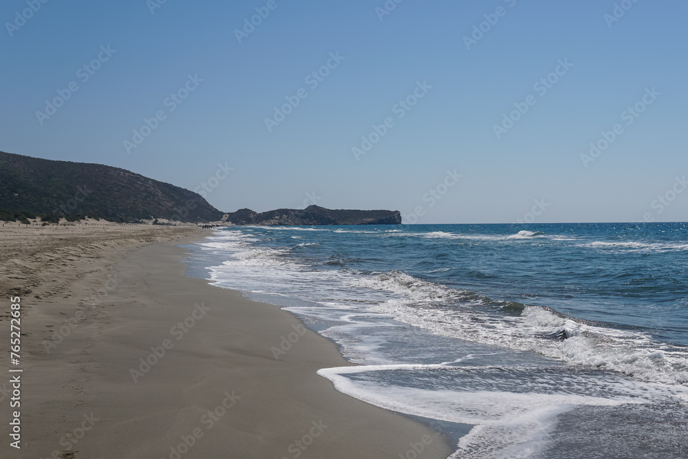 Beach with white sand and blue clear water, mountains in the background, bright blue sky, sunny day
