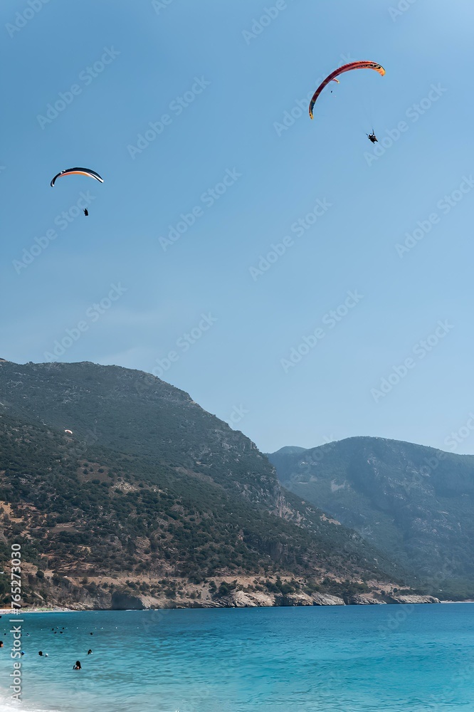 paragliders flying over the sea in front of mountains, with a clear blue sky, blue lagoon in the background, sunny day with no clouds paragliders flying over the sea in front of mountains, with a clear blue sky, blue lagoon in the background, sunny day with no clouds