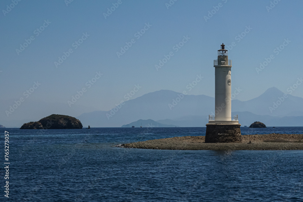 A lighthouse on a small island, the background features a clear blue sky and mountains, clear water