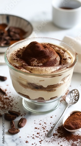 A glass dessert bowl filled with layers of creamy tiramisu, topped with cocoa powder