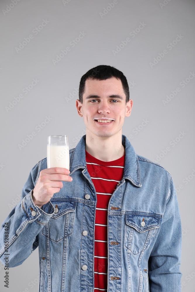 Happy man with milk mustache holding glass of tasty dairy drink on gray background Happy man with milk mustache holding glass of tasty dairy drink on gray background