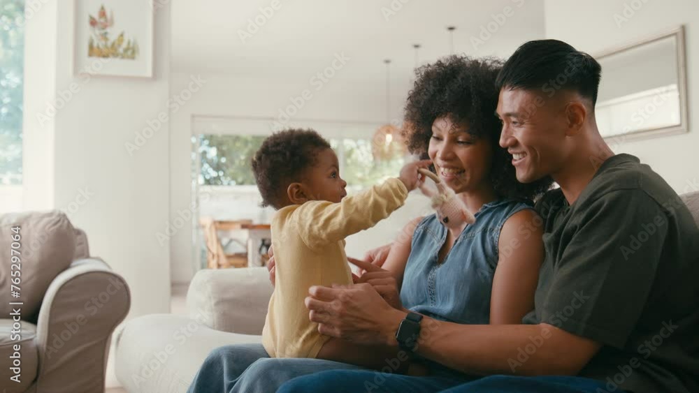 Family shot with parents playing with baby daughter sitting on sofa at home together - shot in slow motion Family shot with parents playing with baby daughter sitting on sofa at home together - shot in slow motion