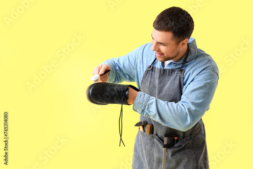 Male shoemaker brushing boot on yellow background