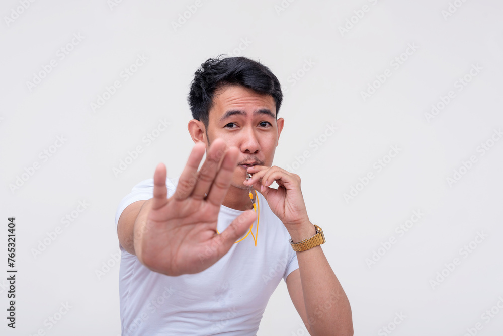 Asian man blowing a whistle and signaling foul play, white background Asian man blowing a whistle and signaling foul play, white background