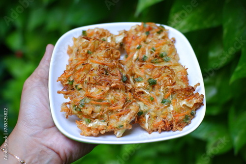 Hand holding a plate of vegetable fritter or bakwan sayur in nature background 