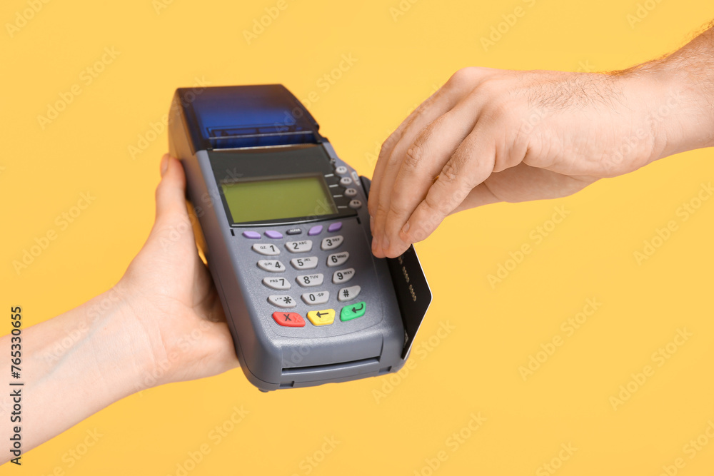 Male hand with credit card and payment terminal on yellow background Male hand with credit card and payment terminal on yellow background
