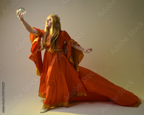 Full length portrait of plus sized woman blonde hair, wearing historical medieval fantasy gown, golden crown of royal queen. Standing pose holding crystal seer orb, isolated studio background.