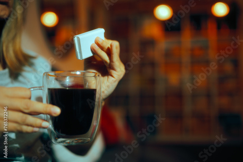 Person Using Artificial Sweetener in her Black Coffee. Adult woman curbing her taste for sweetness with healthier alternatives 
