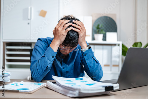 depressed, despair, unhappy, document, executive, exhaustion, sadness, frustration, bad, job. A man is sitting at a desk with a laptop and a stack of papers. and he is in a state of distress.
