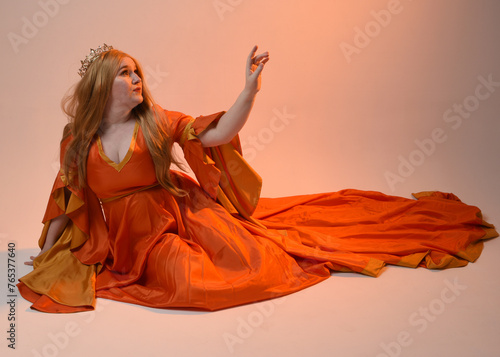 Full length portrait of plus size blonde woman, wearing historical medieval fantasy gown, golden crown royal queen. sitting pose isolated studio background.
