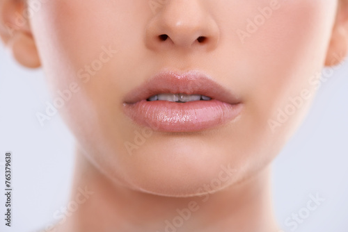 Closeup, face and lips with woman for beauty, makeup with shine and cosmetics for dermatology on white background. Skin, lipstick or balm for moisturizer, skincare and glow for wellness in studio