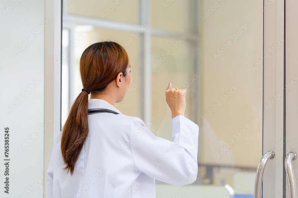 Fototapeta premium Back view of Young female doctor knocking on door