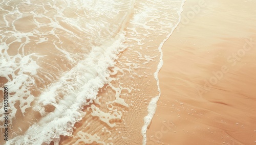 Gentle waves wash over a sandy beach in a warm, sunlit aerial view.