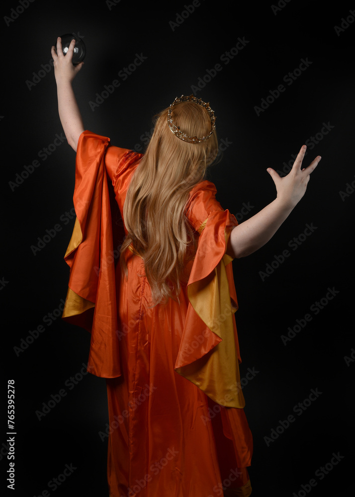Fototapeta premium close up portrait of plus sized blonde woman, wearing historical medieval fantasy gown, crowned royal queen. posing holding magic crystal seer orb, isolated dark black studio background.
