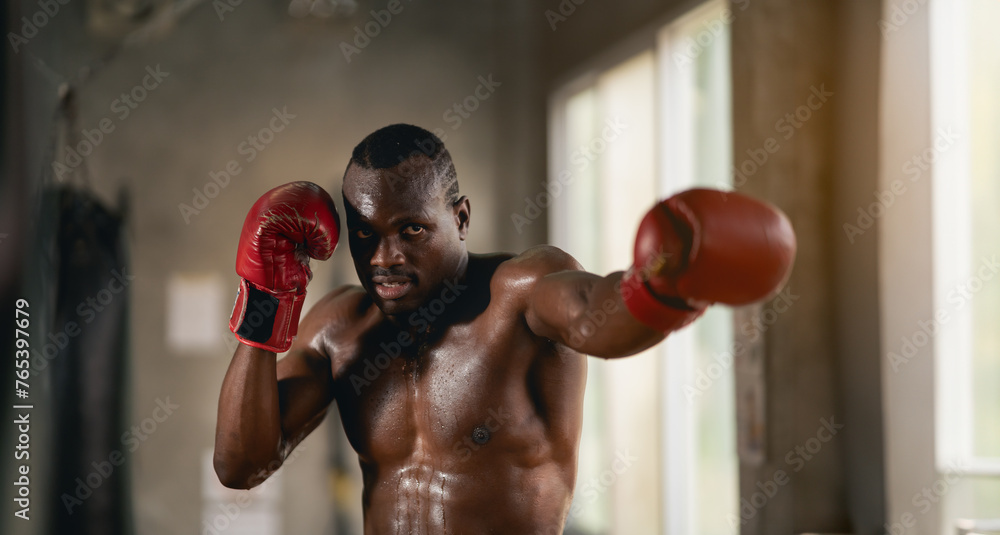 A man in a boxing ring with sweat on his face. He is wearing a red glove. Scene is intense and focused