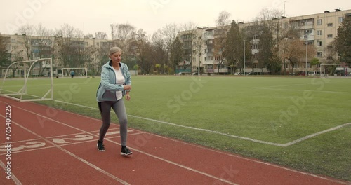 Old fit woman running marathon at stadium arena