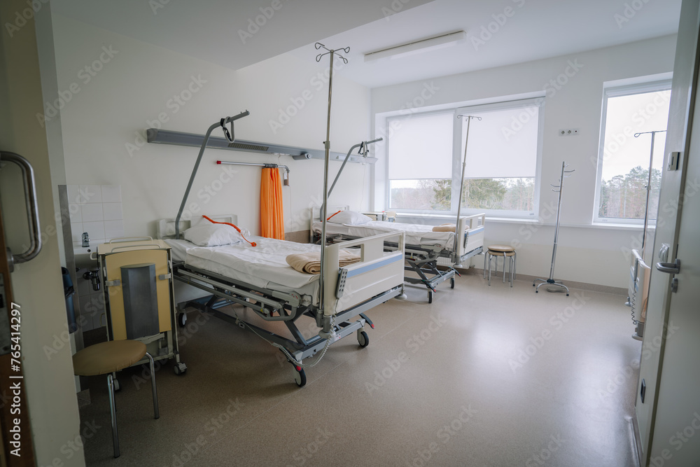 Valmiera, Latvia - March 20, 2024 - A hospital room with two empty beds, IV stands, a chair, large windows with a view, and various medical equipment. Valmiera, Latvia - March 20, 2024 - A hospital room with two empty beds, IV stands, a chair, large windows with a view, and various medical equipment.