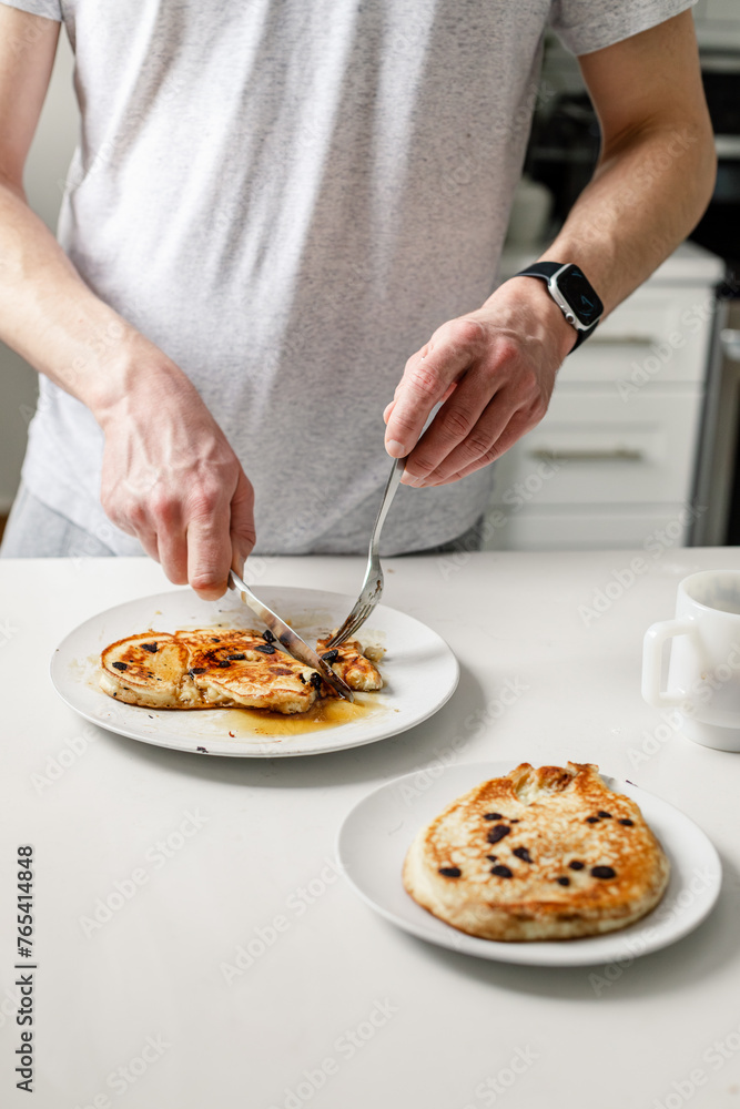 man cutting into homemade pancakes with maple syrup