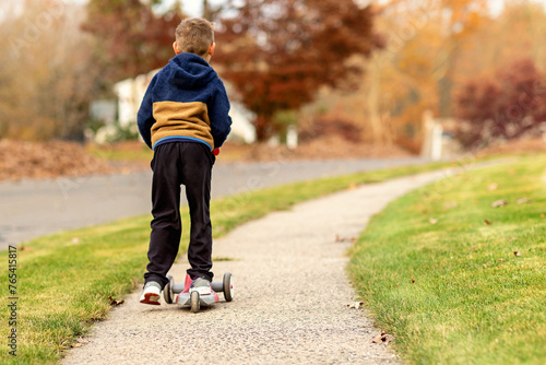 Boy riding scooter on neighborhood sidewalks in the fall photo